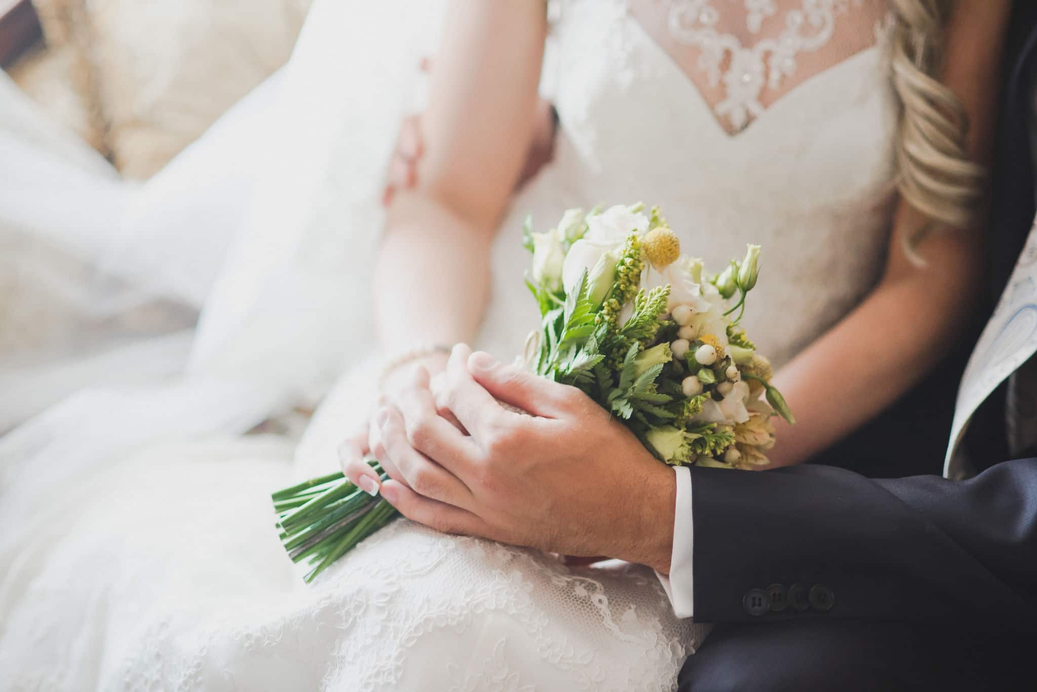 groom holds his bride's hand on a background of lake