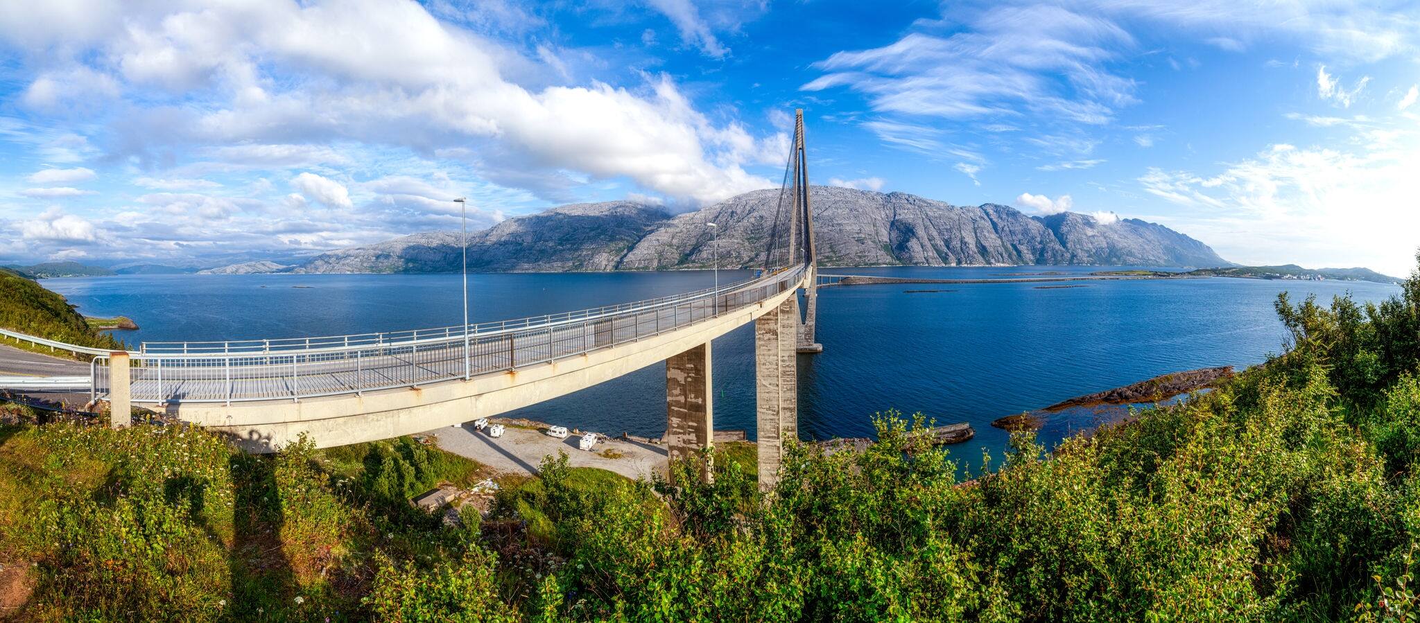Panoramic view at Helgeland Bridge over blue wide river and Seven Sisters mountain range in summer sunny day under blu sky. bridges between Alstahaug and Leirfjord at Helgeland, Norway. At Sandnessjoe