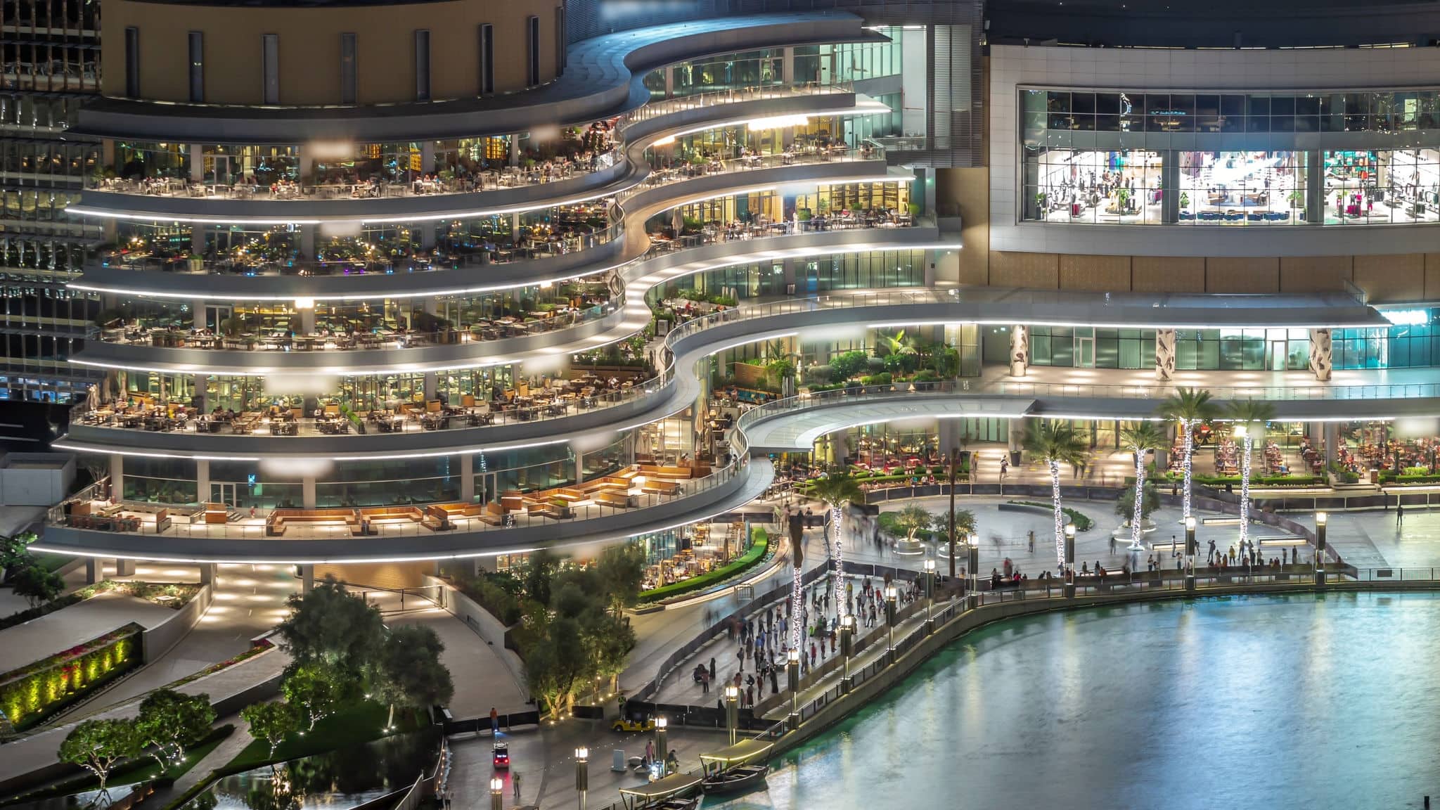 Shopping mall balcony with reataurants near fountain in Dubai downtown aerial night timelapse, United Arab Emirates. Illuminated waterfront walking area