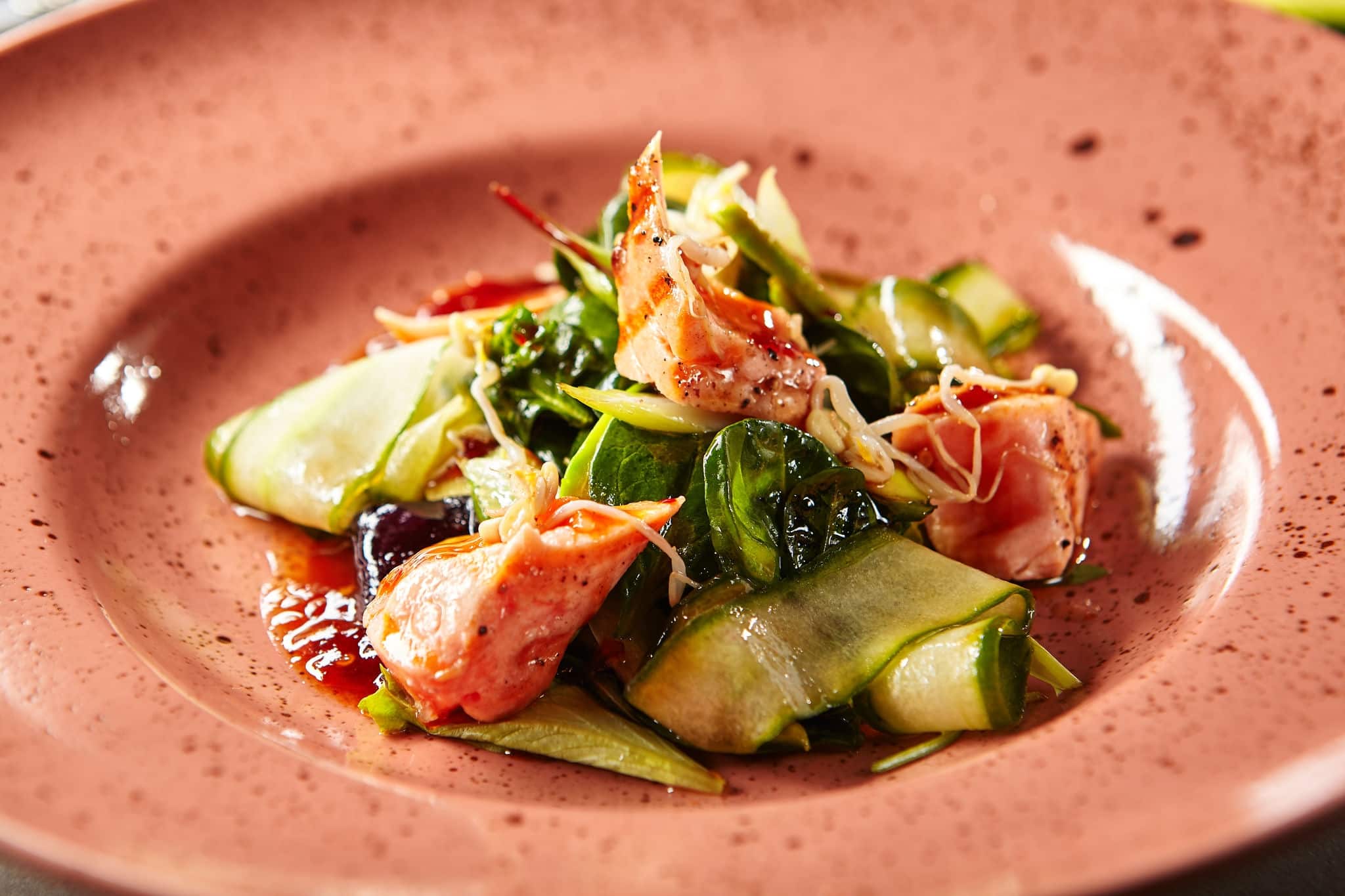 Close-up portrait of juicy salad with avocado smoked salmon and celery. Healthy food in rustic style concept. Served on trendy pink round shaped plate