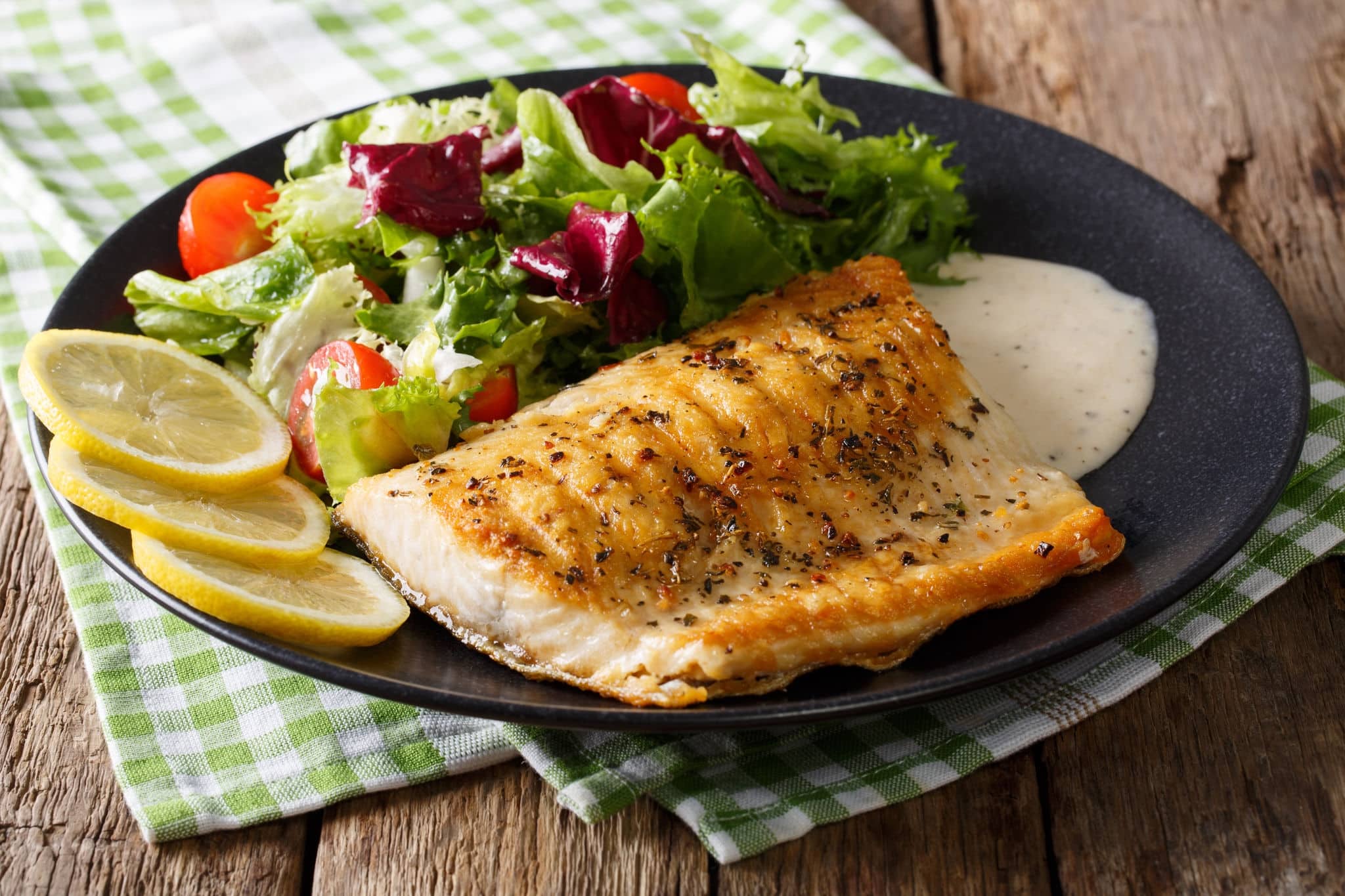 Grilled Arctic char fillet with mixed salad and sauce on a plate close-up. horizontal