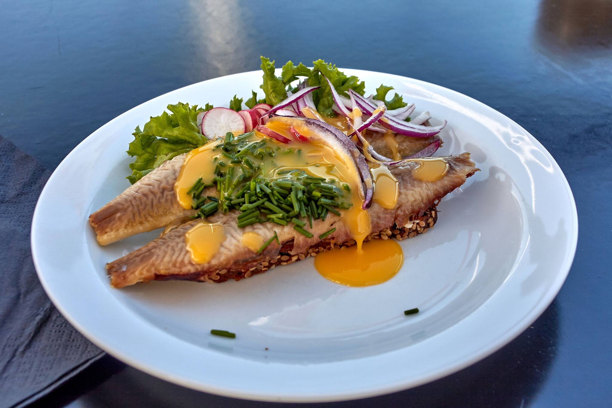 Sol over Gudhjem (Sun over Gudhjem) - traditional Danish sandwich with rugbrod, smoked herring, lettuce, onion, raddish, chives and a raw egg yolk on top, Bornholm island, Denmark.