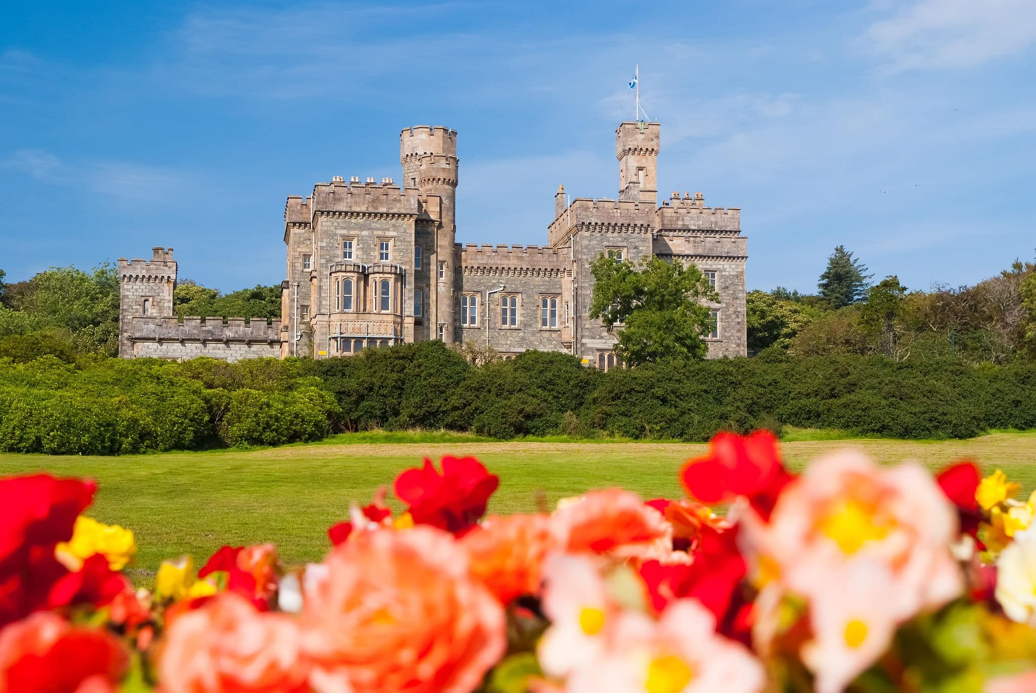 Lews Castle in Stornoway, United Kingdom with blurred roses in foreground. Castle with green grounds on blue sky. Historic architecture and design. Landmark and attraction. Summer vacation on isle.