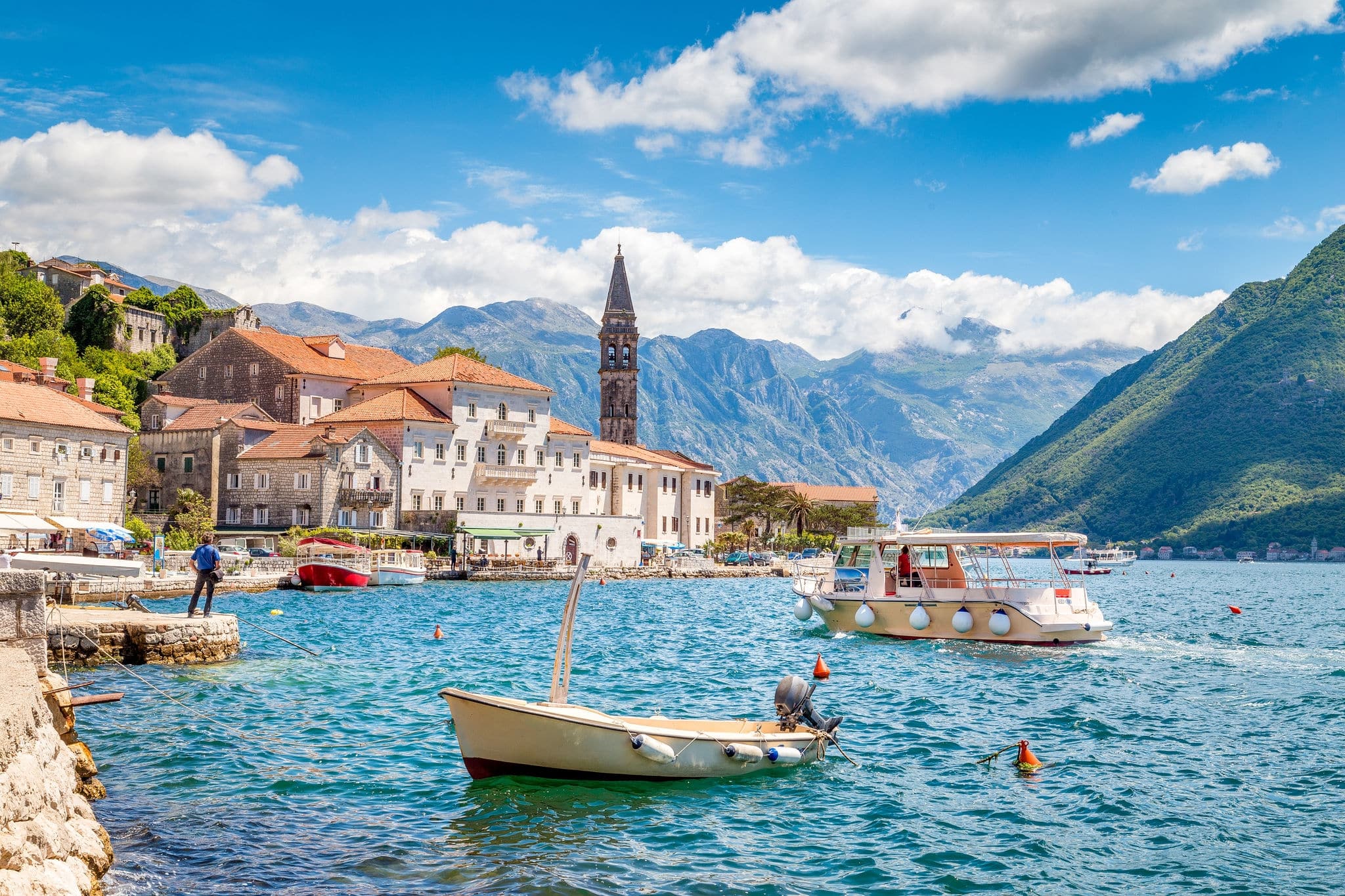 Scenic panorama view of the historic town of Perast at famous Bay of Kotor with boats on a beautiful sunny day with blue sky and clouds in summer, Montenegro, southern Europe