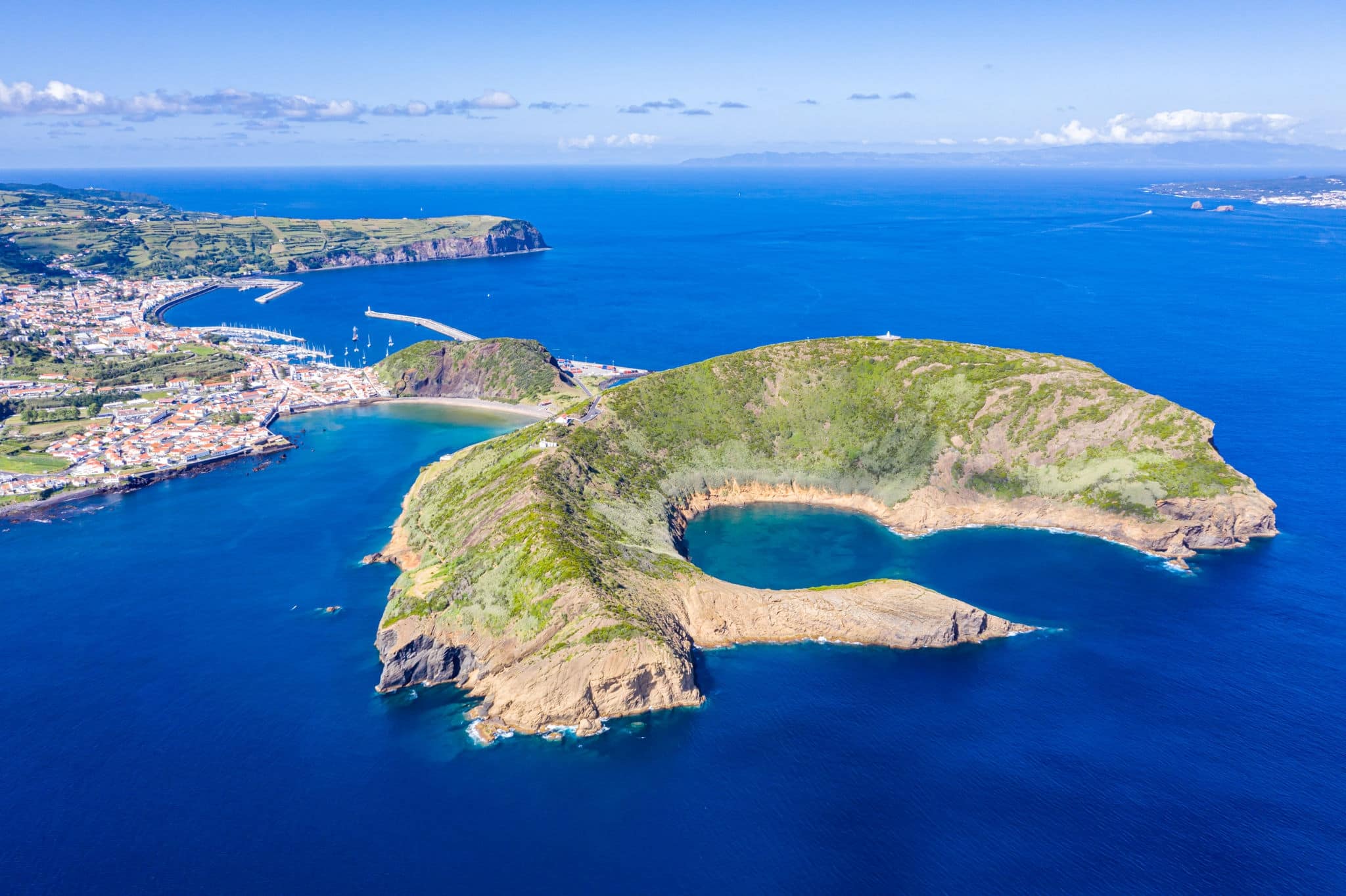Nature Park of destructed extinct volcano craters of Caldeirinhas, mountain Guia, baia (bay) do Porto Pim and port, beaches, marinas, red roofs of historical Horta city, Faial island, Portugal.
