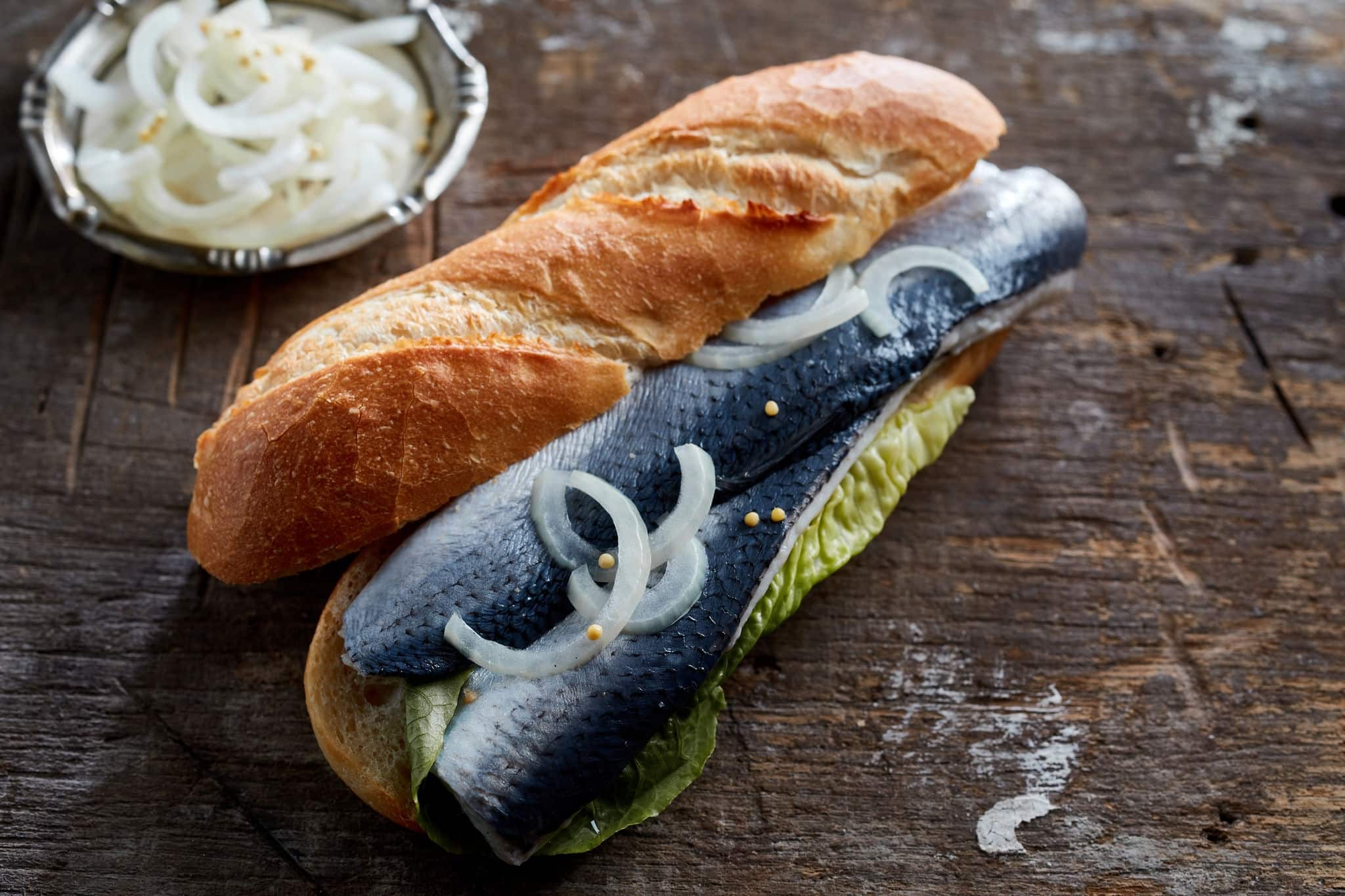 From above of delicious traditional German sandwich Fischbrotchen made with crunchy baguette bread stuffed with marinated herring fish fillet with onion and lettuce on shabby wooden table