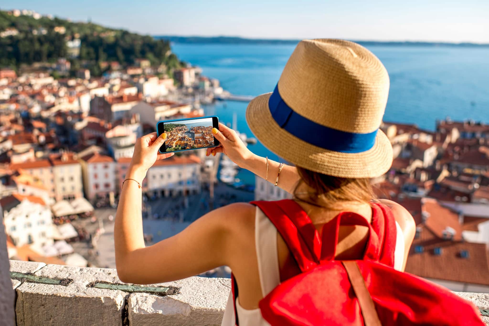 Young female traveler with red backpack and photo camera enjoying the view on Piran old town. Traveling in Slovenia