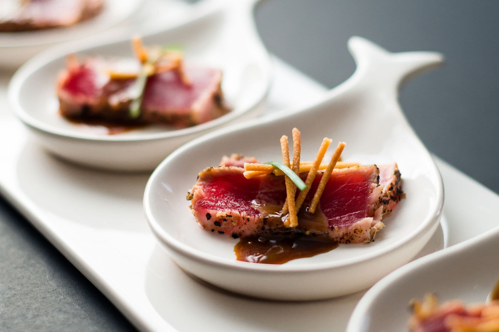 Tuna Tataki is a Japanese dish which consist of briefly seared tuna steak in thin slices. Served as appetizer with brandy sauce and garnish on a dark background.