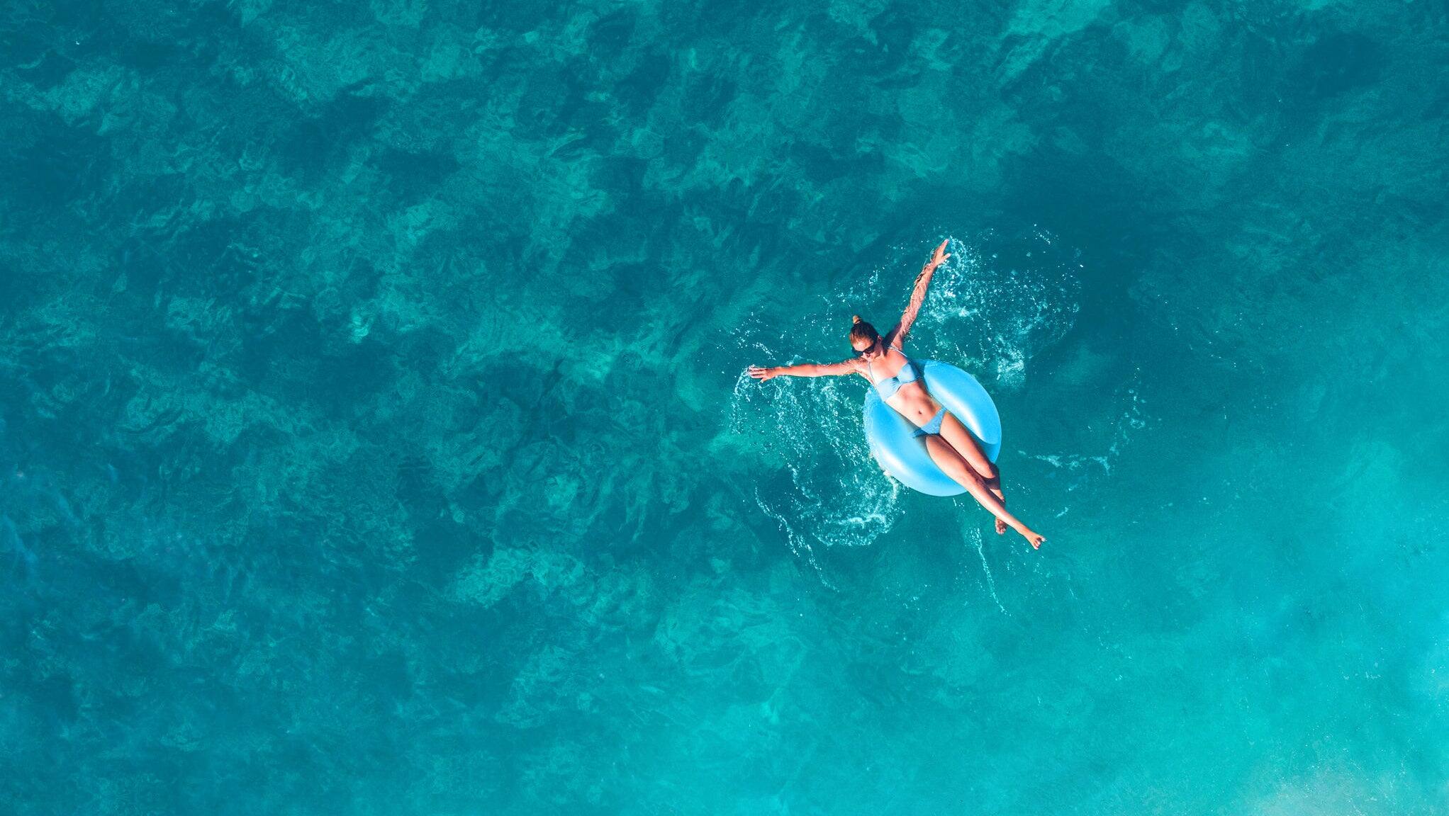 High angle view photo of a young woman relaxing while floating in the ocean using swimming tube; wide photo dimensions