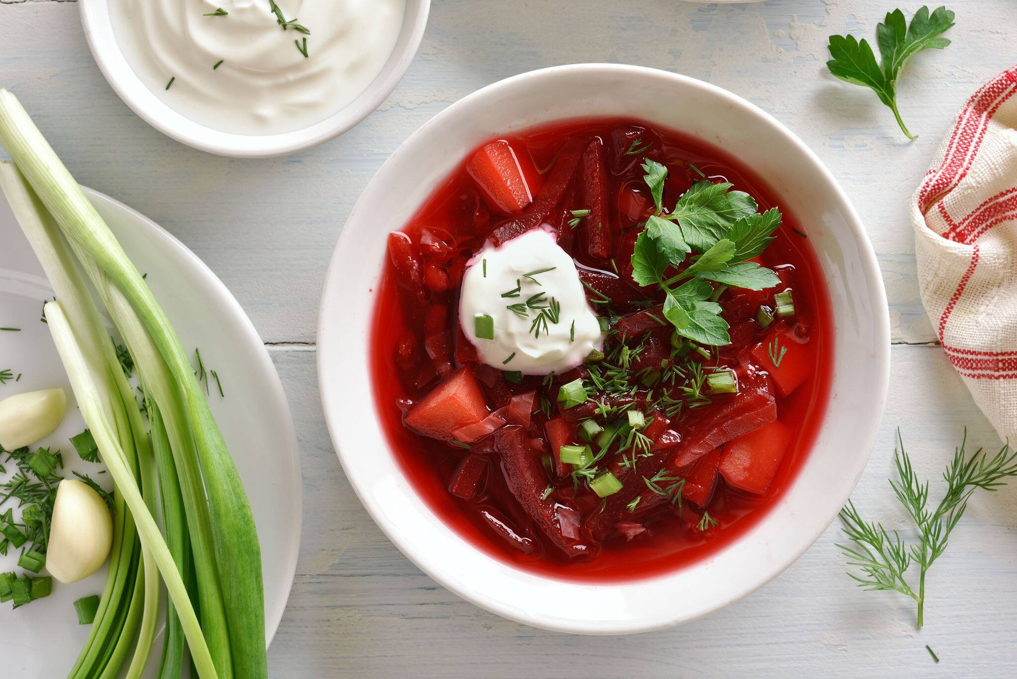 Tasty beetroot soup in bowl on white wooden background. Traditional ukrainian russian soup (borscht) with greens and sour cream. Top view, flat lay