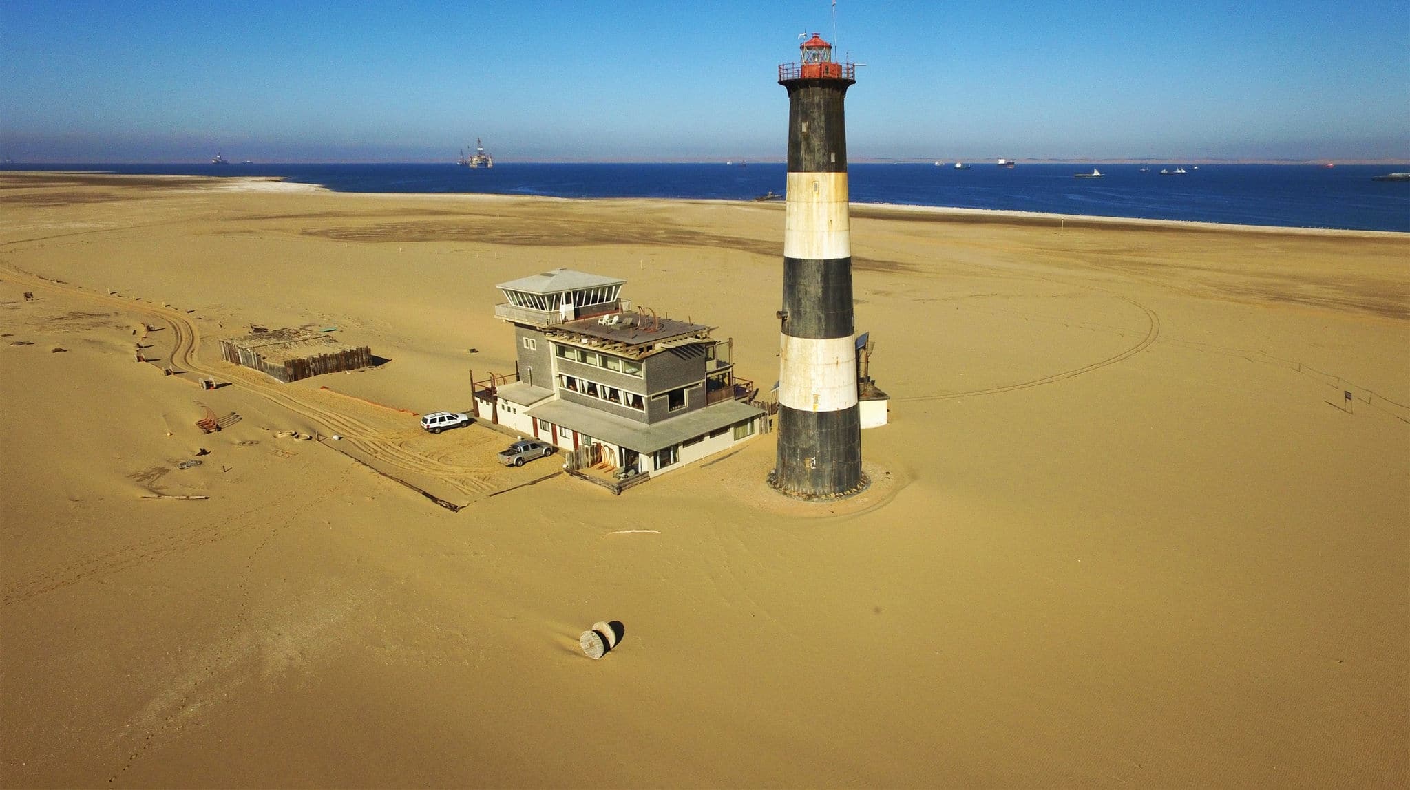 High quality aerial drone photo of desert sand peninsula, old lighthouse, old power station building on seals beach, Walvis Bay lagoon with sea ships at Namibia's Atlantic west coast, southern Africa