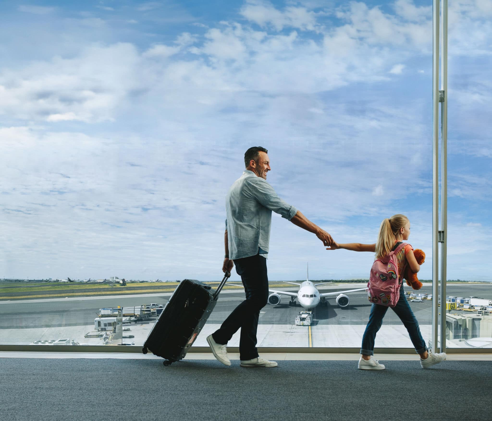 Girl holding hand of her father and walking to board their flight at airport. Father and daughter going on a vacation.