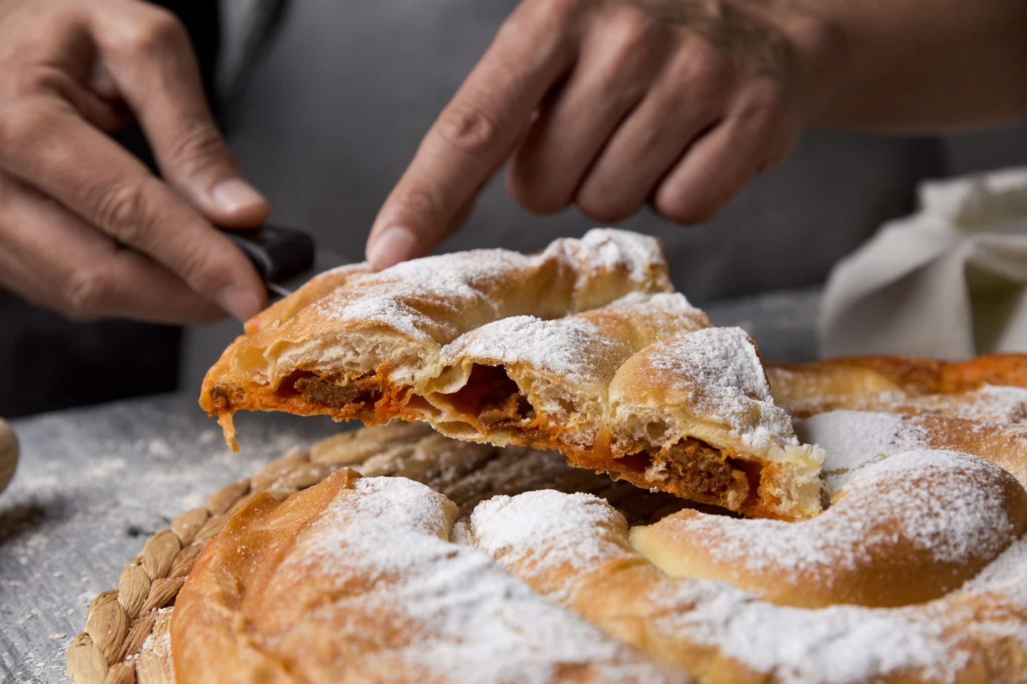 closeup of a young caucasian man serving a piece of on an ensaimada, a pastry typical of Mallorca, Spain, filled with sobrasada, placed on a rustic wooden table
