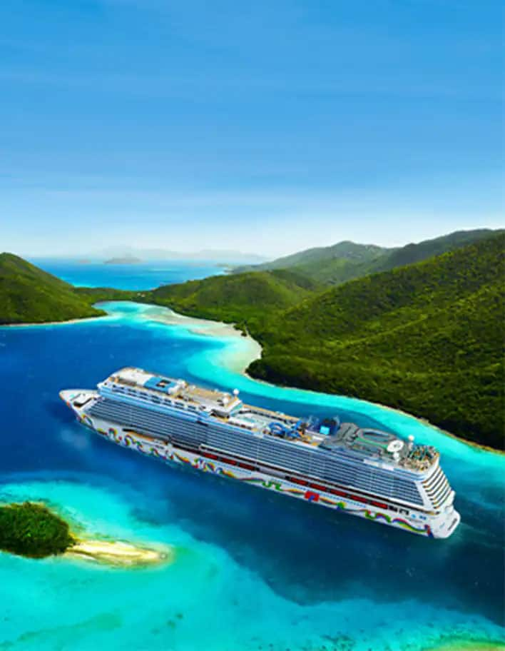 Aerial look of the Norwegian Encore sailing into clear blue ocean water in between green hills