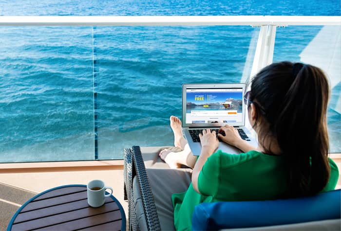 Frau benutzt Laptop auf dem Balkon einer Kabine von Norwegian