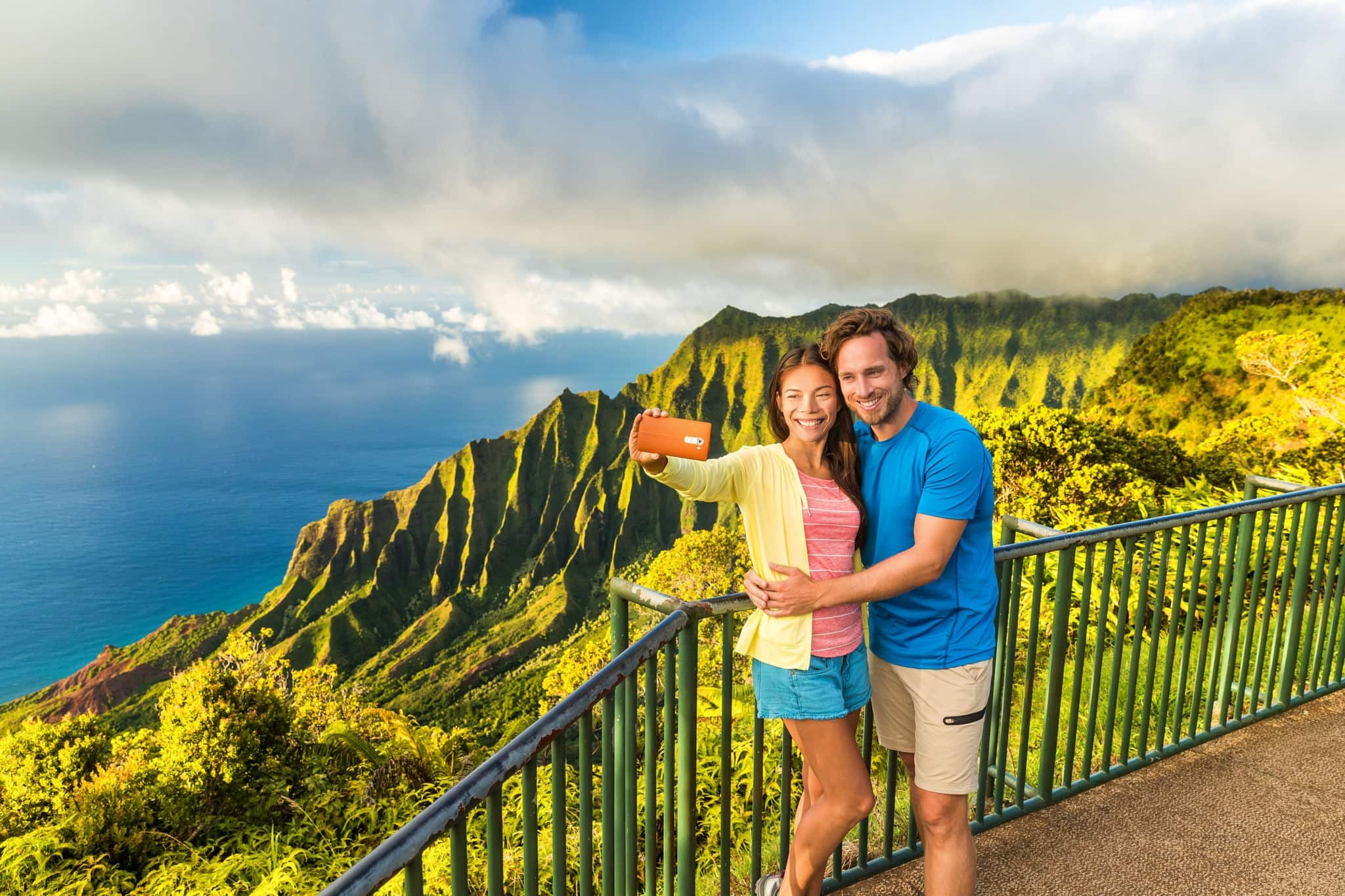 667106167 Hawaii travel Napali selfie couple at Napali nature Kauai Hawaii. Young tourists taking selfie phone photo at Na Pali lookout in Kauai, Hawaii. Travel people at famous Kalalau hawaiian attraction.