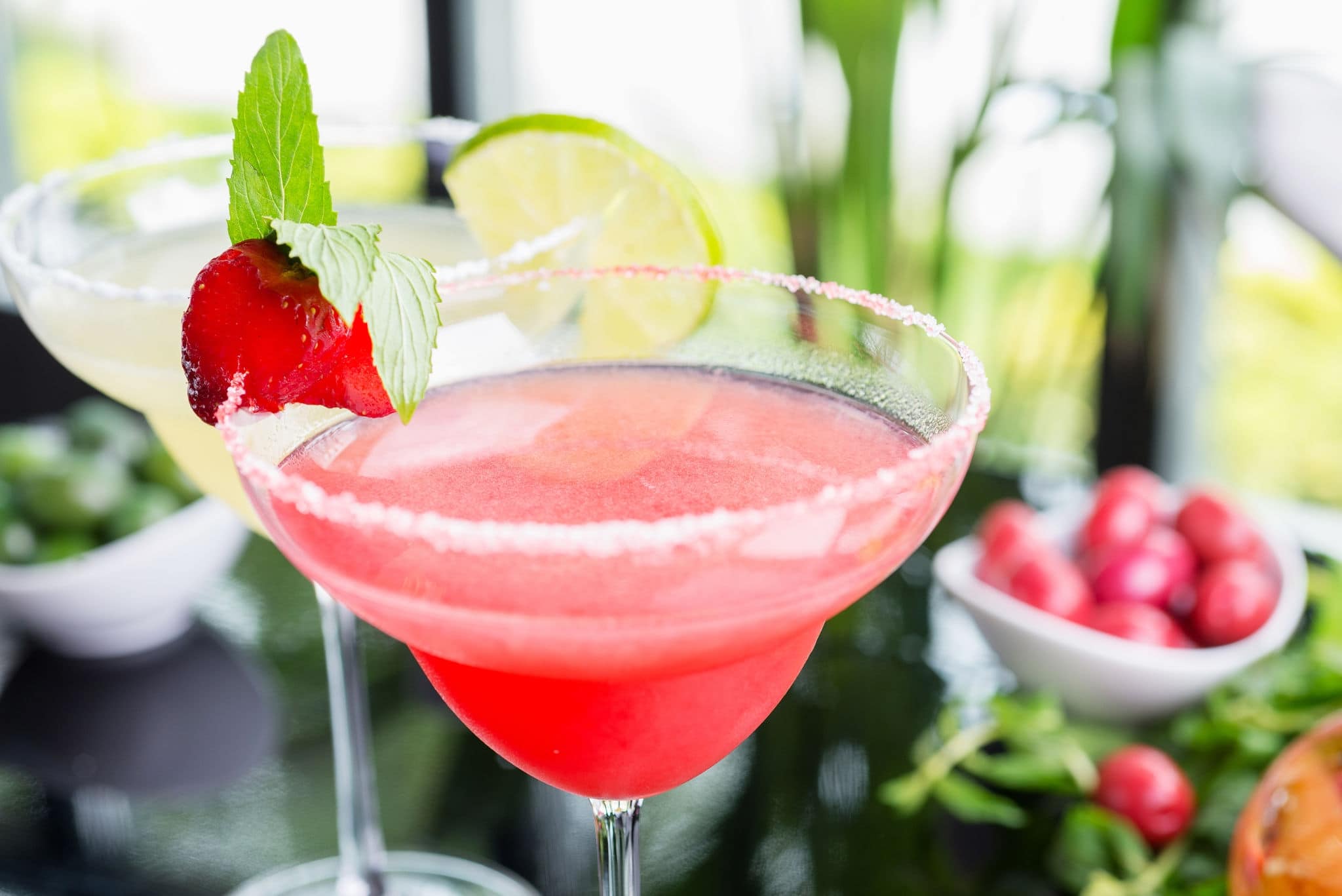 NCL-Lifestyle-Cruise-Cocktails-Strawberry-Lime-Blog mix of the bright refreshing cocktails lime and strawberry daiquiri on a table in a restaurant with decoration of salt on the edge of the glass with fresh mint and lime slices and berries. soft focus